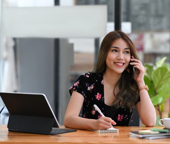 smiling woman talking on the phone and making notes on notebook.